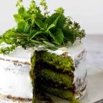 a sliced three layered green cake covered with whipping cream frosting, with a chocolate ganache and decorated with fresh herbs like mint, rosemary and thyme
