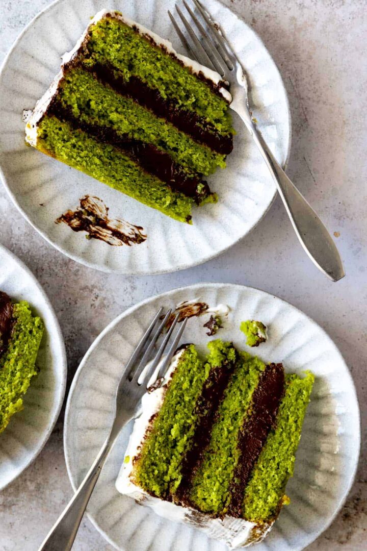 3 plates with slices of a three layered green cake with chocolate ganache and whipped cream frosting