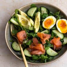 a bowl with mixed greens, avocado, boiled egg, cucumber and smoked salmon