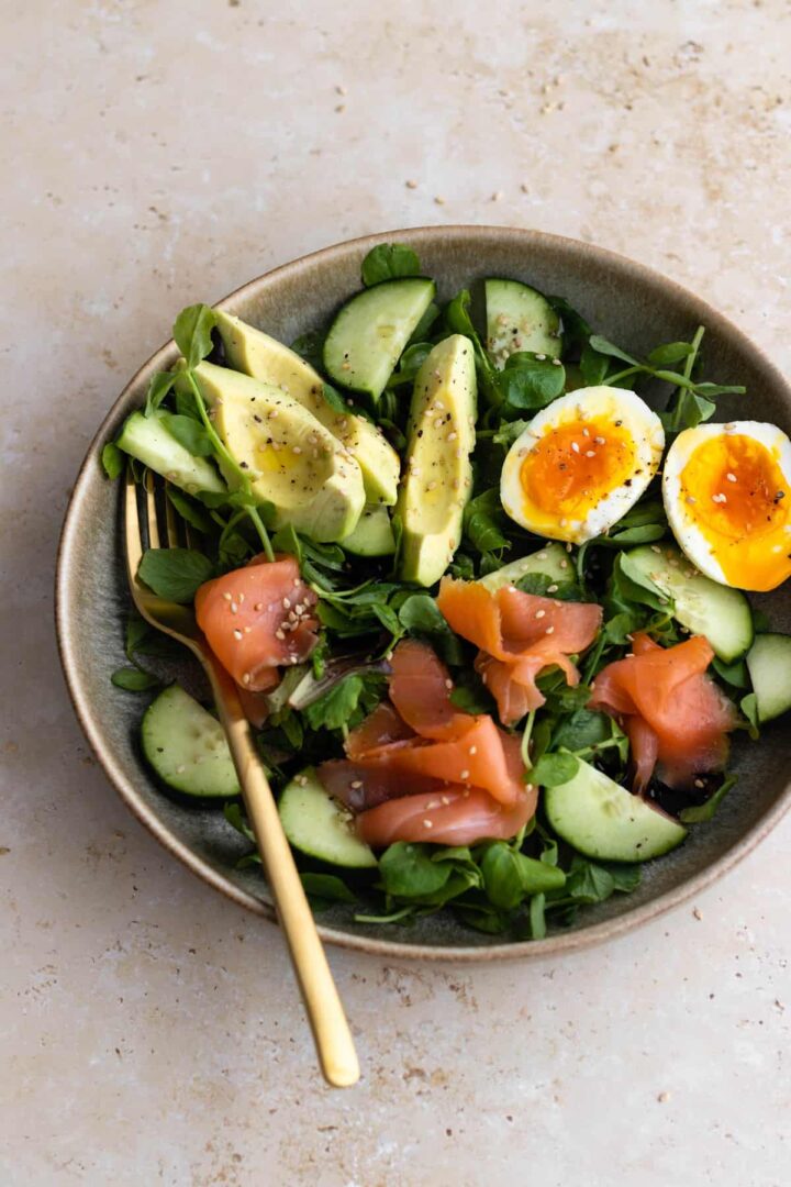 a bowl with mixed greens, avocado, boiled egg, cucumber and smoked salmon