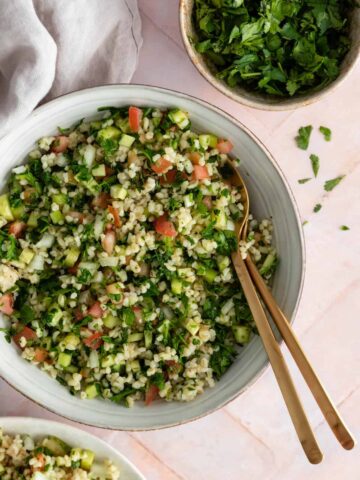 a bowl with tabbouleh salad, a small plate served with salad, and a smaller bowl with coriander on the side