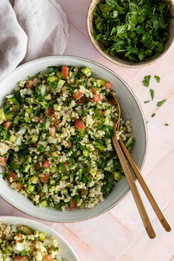 a bowl with tabbouleh salad, a small plate served with salad, and a smaller bowl with parsley on the side
