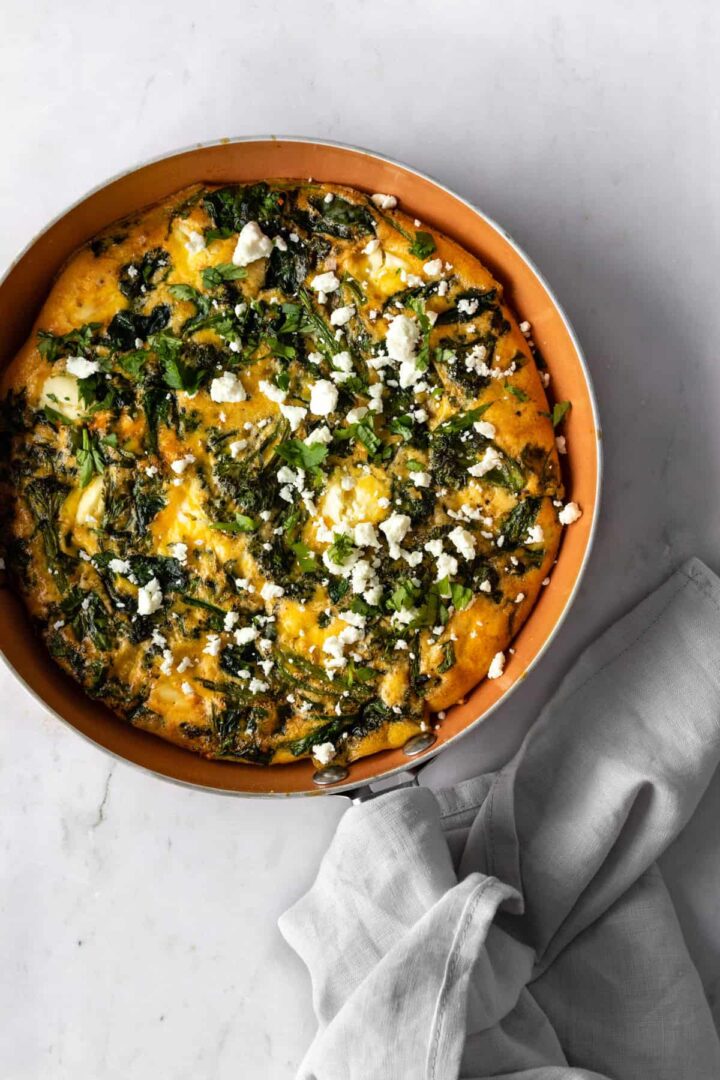 frittata on a oven-safe pan with crumbled feta cheese on top