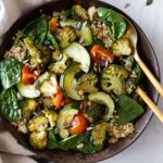 a bowl with roasted vegetables, spinach leaves, quinoa, pumpkin seeds, sunflower seeds. A small bowl with more pumpkin seeds on top of a marble board