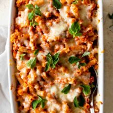 a baking dish with baked ziti garnished with fresh oregano leaves