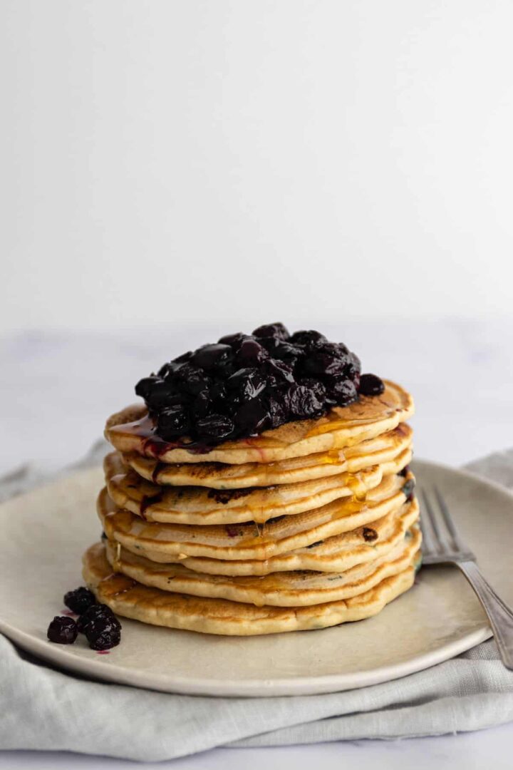 a plate with a stack of pancakes with blueberries and maple syrup on top