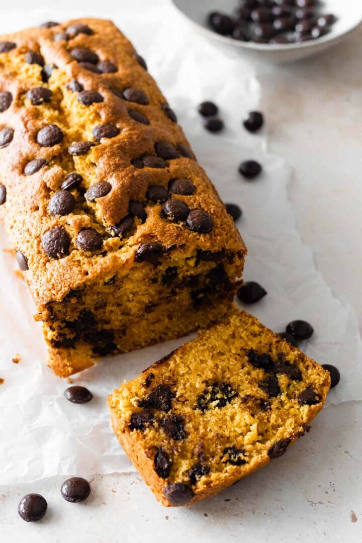 chocolate chip pumpkin bread on top of parchment paper with one slice and a bowl with chocolate chips on the side