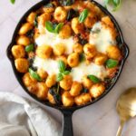 a skillet with gnocchi bake, garnished with fresh basil and a gold spoon on the side