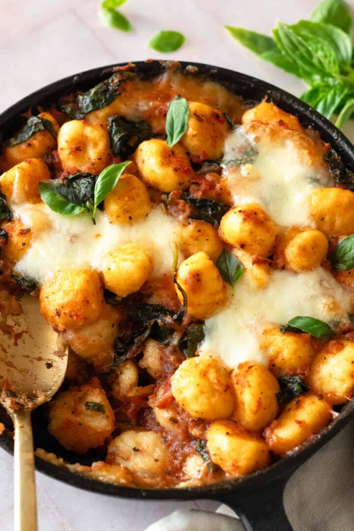 a cast iron skillet with baked gnocchi garnished with fresh basil leaves