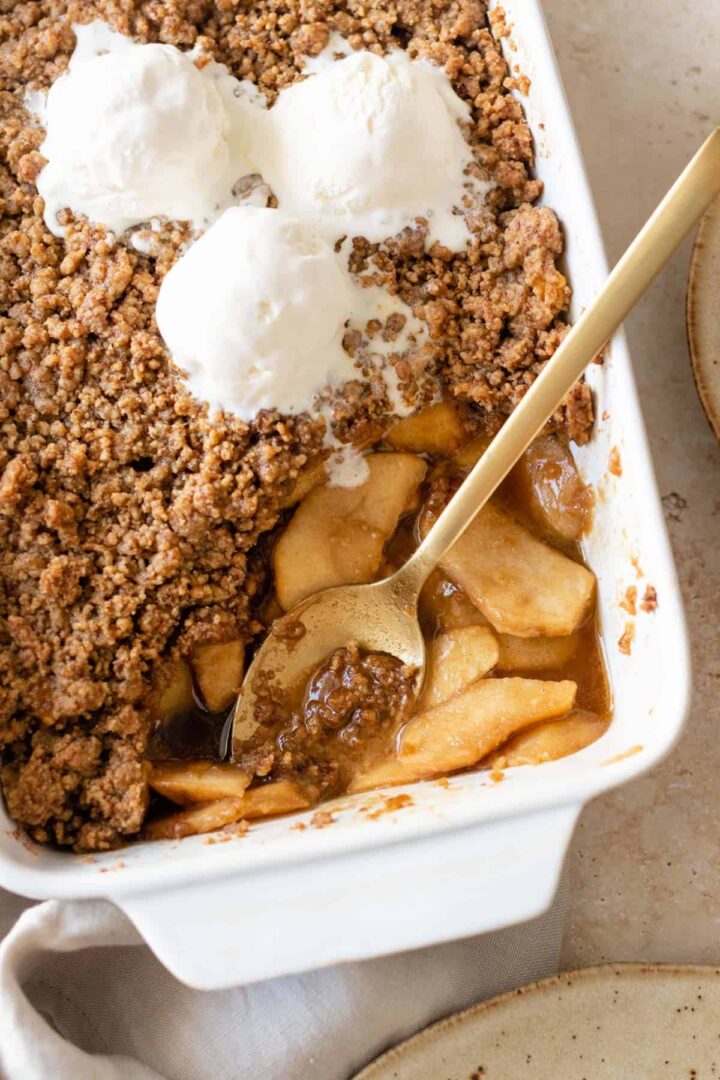 a baking dish with apple crumble and three ice cream bowls on top and a gold spoon
