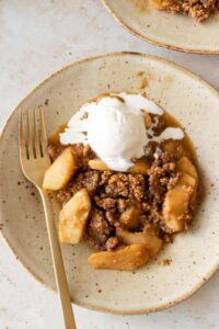 a plate served with apple crumble and one bowl of ice cream melting on top