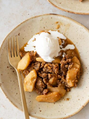 a plate served with apple crumble and one bowl of ice cream melting on top