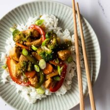 a plate served with white rice, chicken stir fry and garnished with sesame seeds and chopped green onions