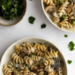 two bowls served with mushrooms, fusilli pasta, vegan cream and garnished with coriander