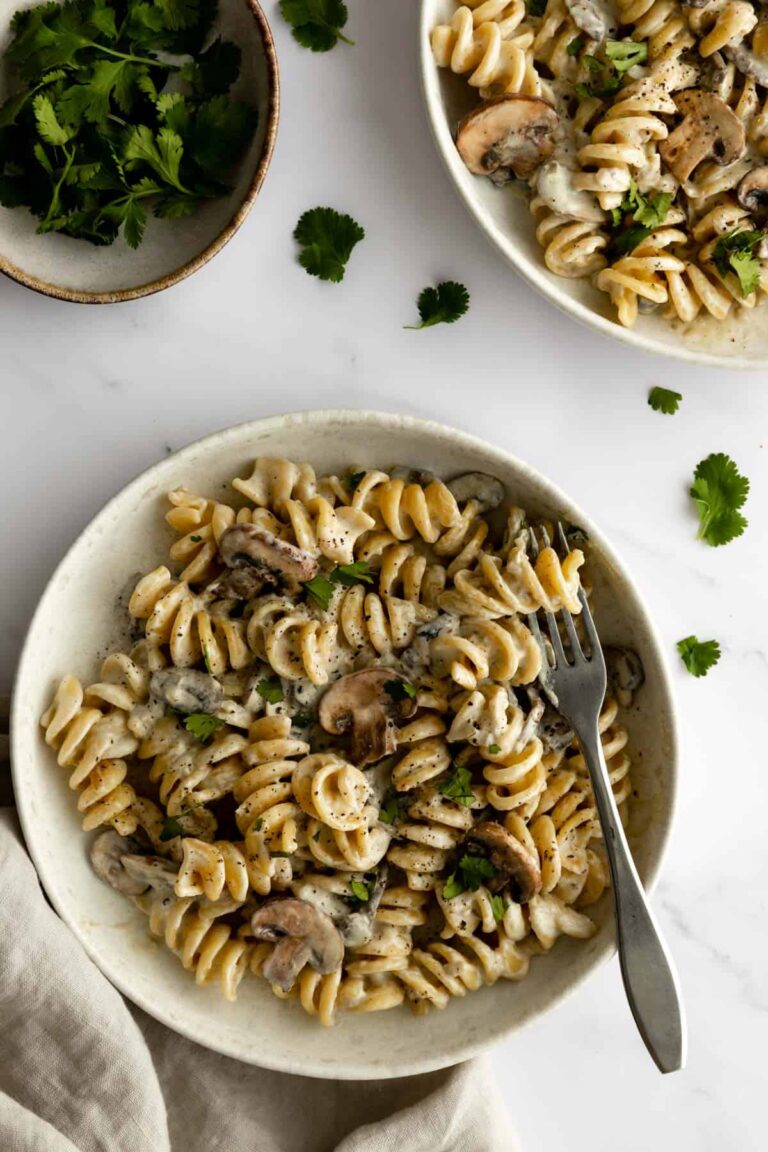 tow bowls served with fusilli pasta, mushrooms, vegan cream and garnished with coriander, a small bowl with coriander on the side