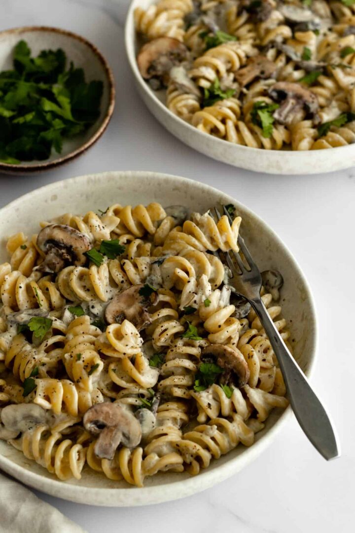 two bowls served with mushrooms, fusilli pasta, vegan cream and garnished with coriander