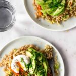 two plates served with quinoa mixed with vegetables, poached egg, sliced avocado and chopped coriander on top