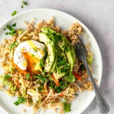 a plate served with quinoa mixed with veggies, poached egg, sliced avocado, garnished with coriander