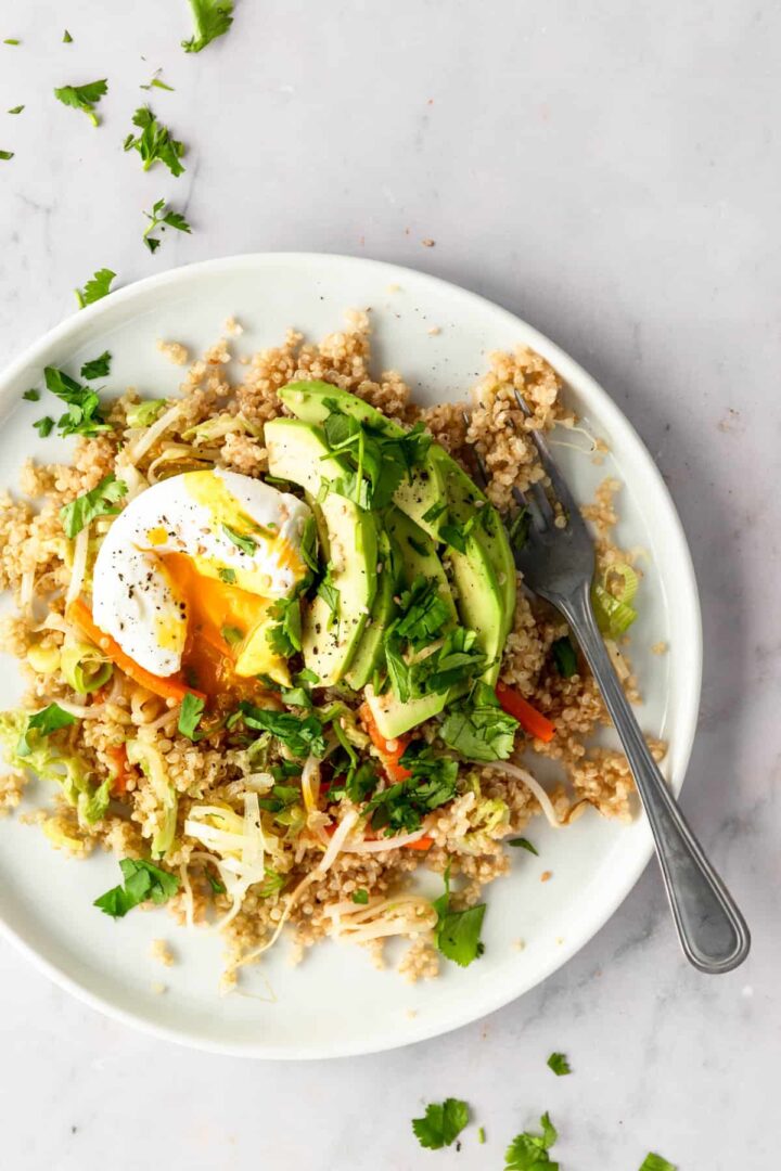 a plate served with quinoa mixed with veggies, poached egg, sliced avocado, garnished with coriander