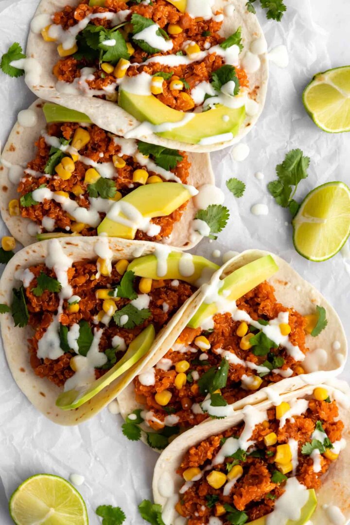 quinoa tacos with sweet corn, sliced avocado, coriander, lime wedges and vegan dressing on top
