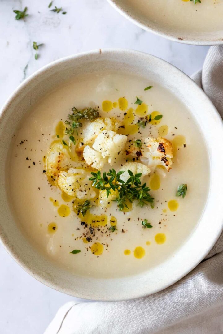 a bowl served with soup and garnished with roasted cauliflower, olive oil, thyme and black pepper