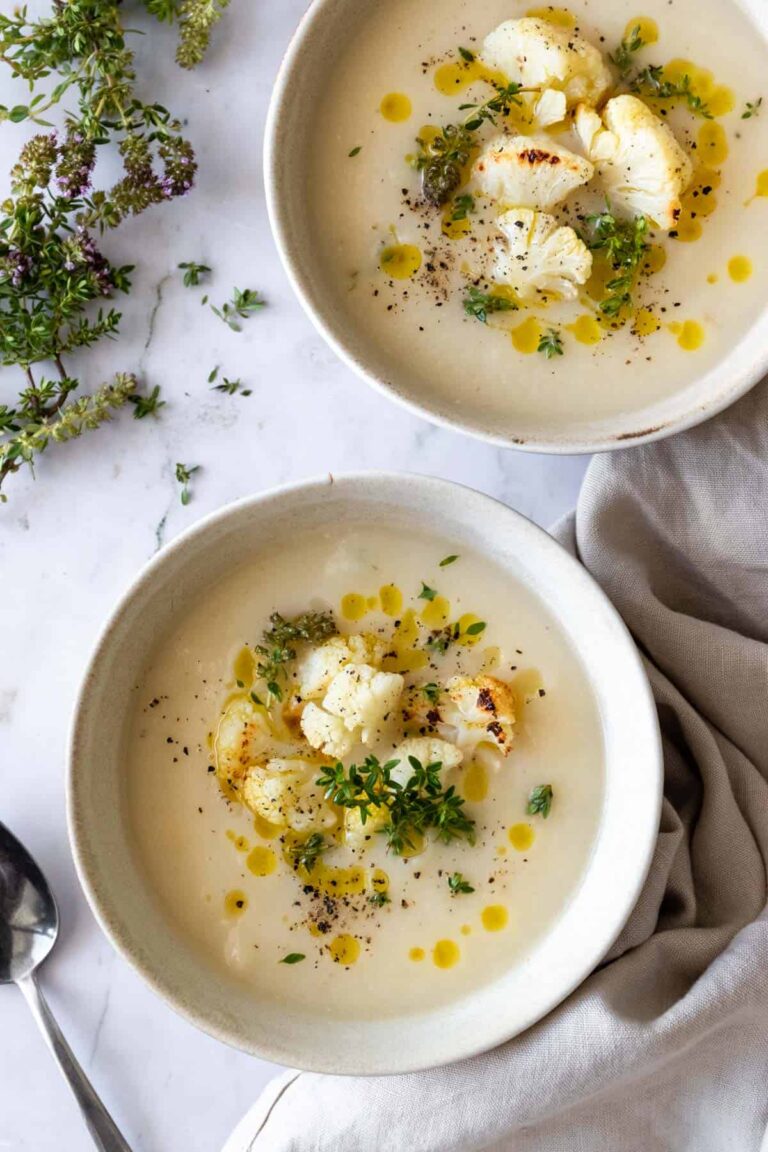 two bowls served with soup and garnished with roasted cauliflower, olive oil, thyme and black pepper