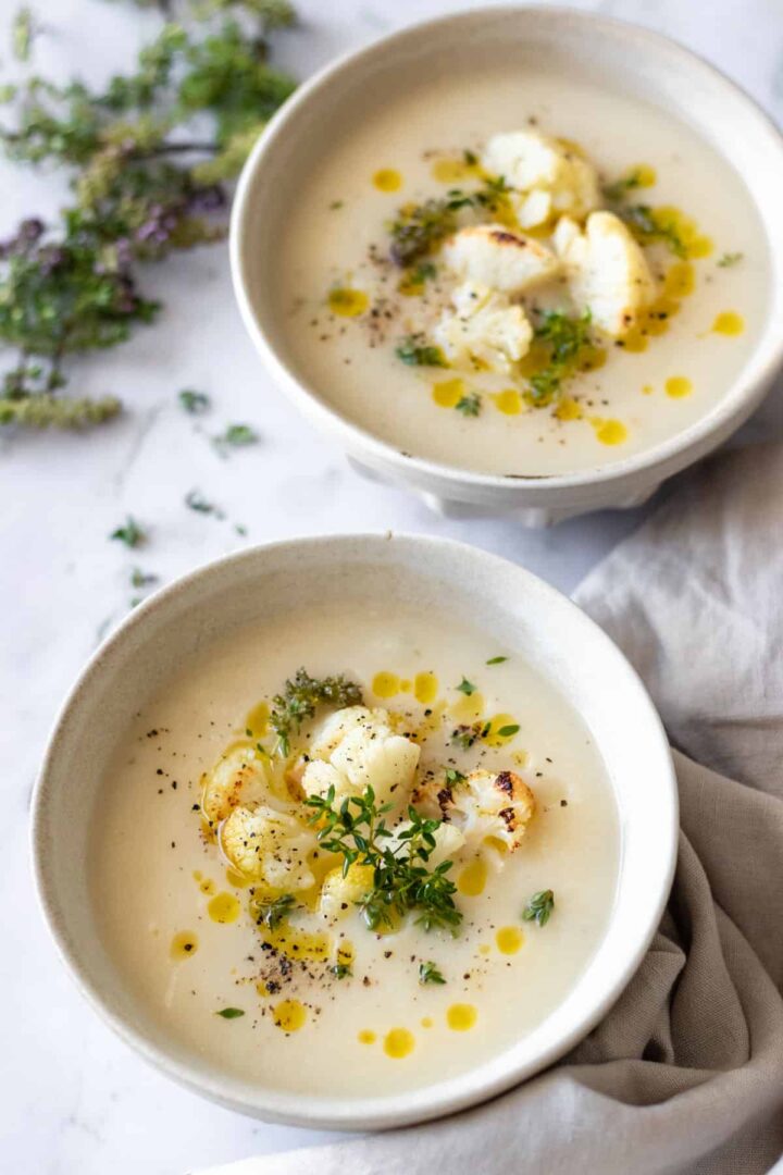 two bowls served with soup and garnished with roasted cauliflower, olive oil, thyme and black pepper