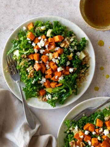 two plates served with quinoa, kale, sweet potato, walnuts, avocado and feta cheese. A bowl with dressing on the side