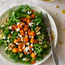 a plate served with quinoa, kale, sweet potato, walnuts, avocado and feta cheese. A bowl with dressing on the side