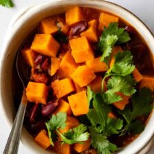 a bowl served with stuffed sweet potato, beans and garnished with coriander