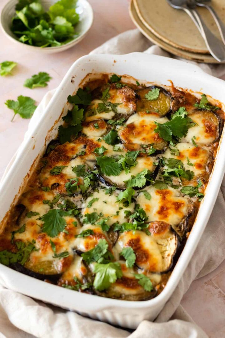 vegetable moussaka on a baking dish with chopped coriander on top, a bowl with more coriander on the side and forks on the bottom left corner