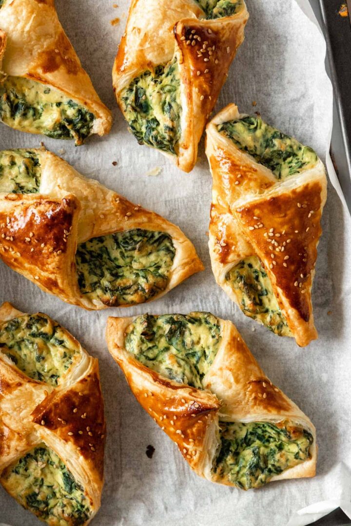 spinach puffs garnished with sesame seeds on top of parchment paper