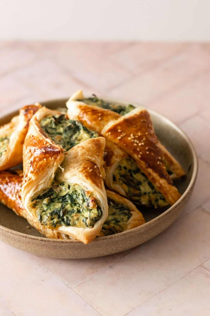 spinach puffs on a plate on top of a pink board