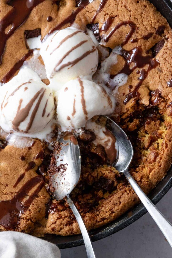 close up of a chocolate chip cookie on a skillet with ice cream and chocolate drizzle on top