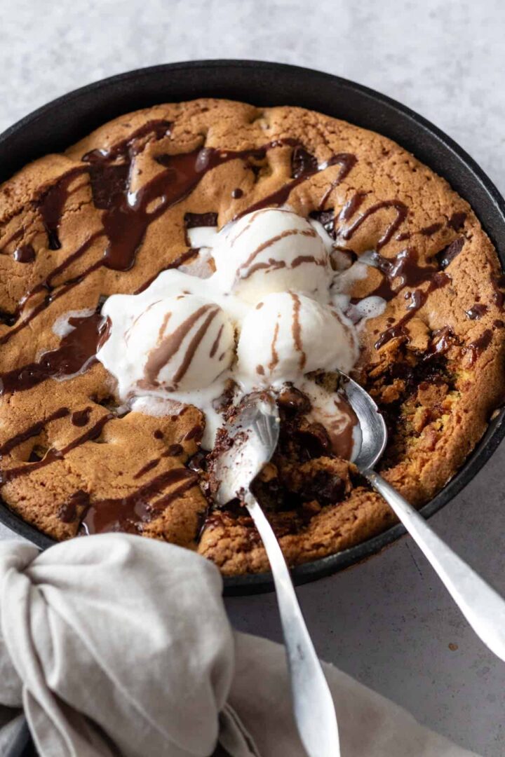 chocolate chip skillet cookie with vanilla ice cream on the top and two spoons