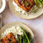 two plates served with baked salmon, white rice, asparagus, sesame seeds and chopped chives