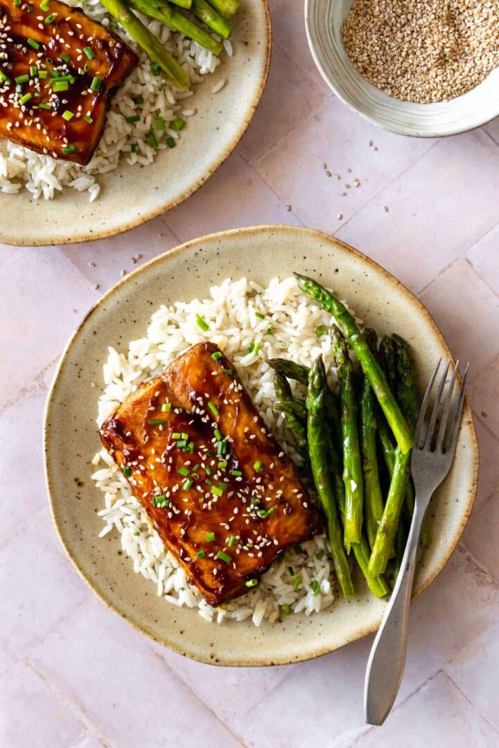two plates served with roasted salmon, white rice, asparagus, chopped chives and sesame seeds