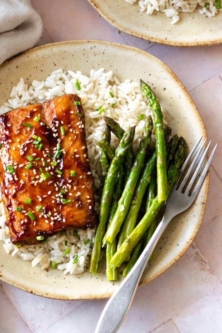a plate served with baked salmon, white rice, asparagus, chopped chives and sesame seeds