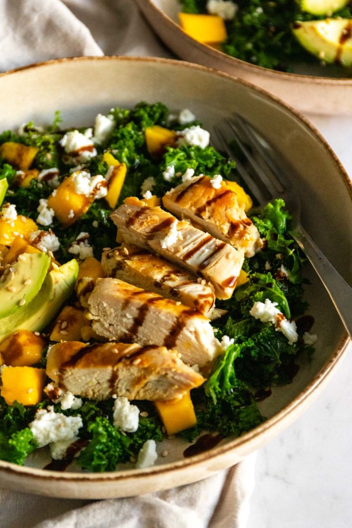 close up of a plate with chicken, kale, avocado, feta cheese, sesame seeds and balsamic glaze
