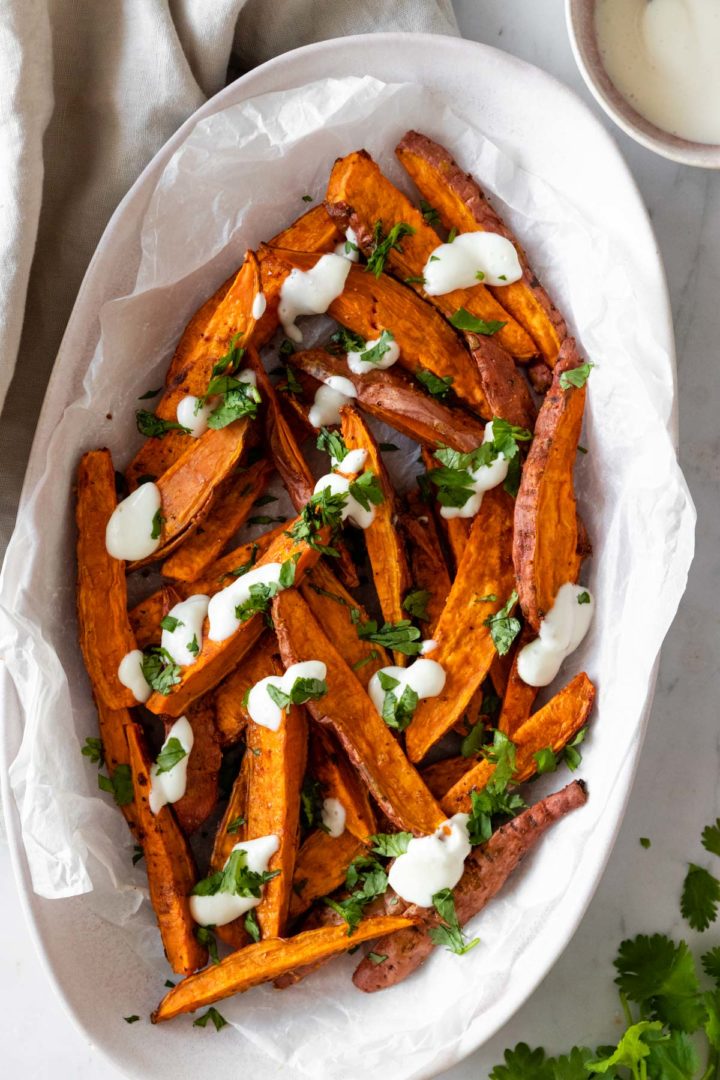 sweet potato wedges on a plate with chopped coriander and garlic dressing