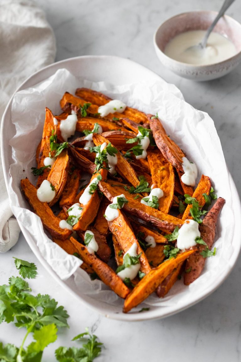 sweet potato wedges on a plate with chopped coriander and garlic dressing. A small bow with more garlic dressing on the side