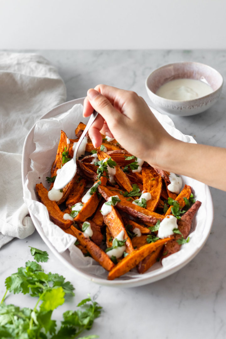 sweet potato wedges on a plate with chopped coriander and garlic dressing