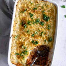 a baking dish with lentil Shepherd's pie, chopped coriander and a spoon