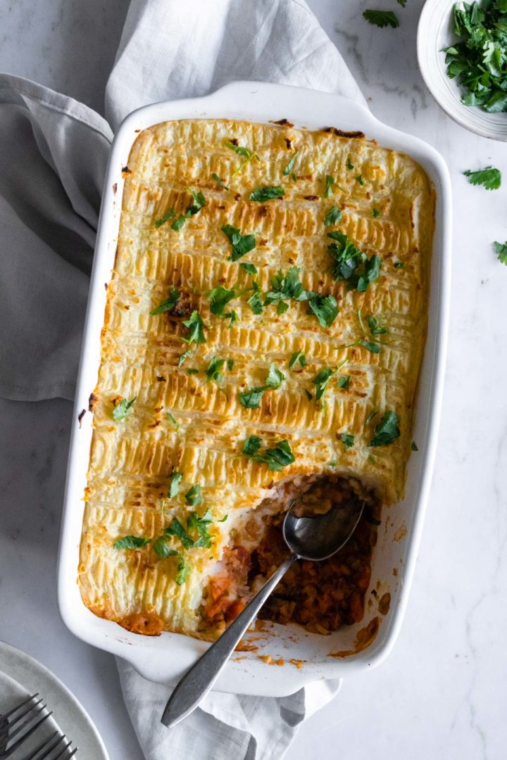 a baking dish with lentil Shepherd's pie, chopped coriander and a spoon