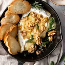 baked brie, toasted bread, walnuts and rosemary inside a black skillet, more rosemary and walnuts on the side