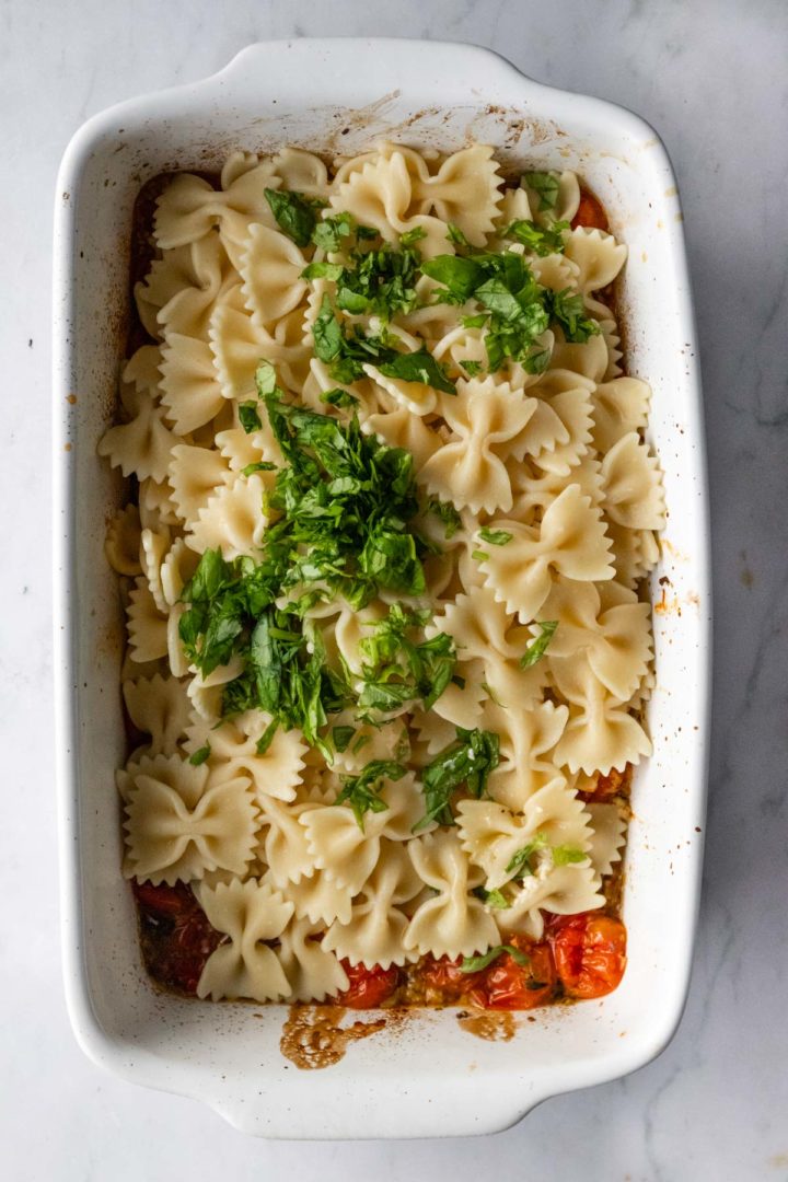 a baking dish with pasta, tomatoes, feta and chopped basil