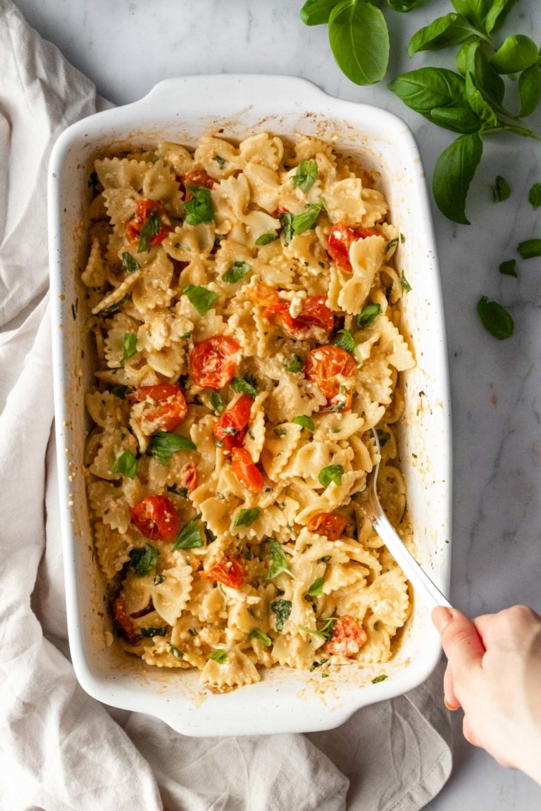 baked feta pasta on a baking dish and a hand holding a spoon