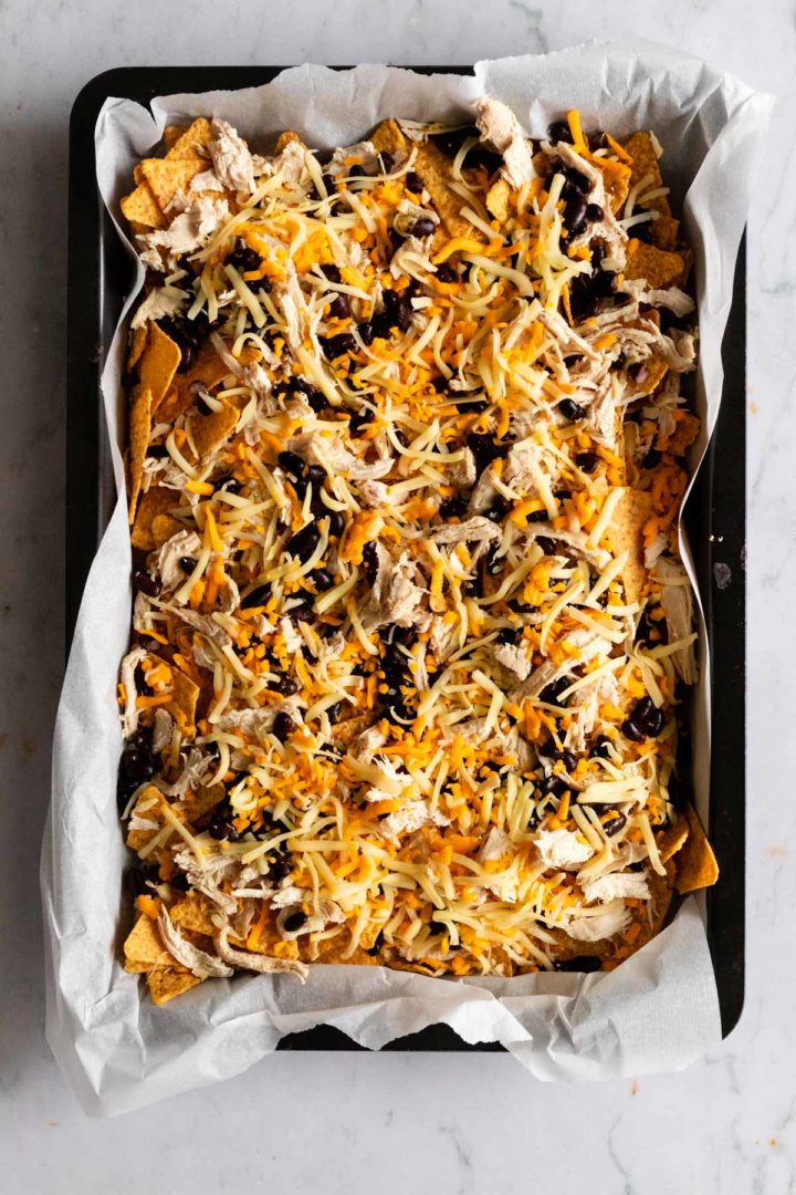 a baking tray with tortilla chips, shredded chicken, cheese and black beans before going to the oven