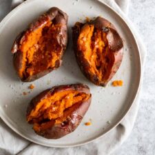 three baked sweet potatoes seasoned with salt and black pepper on a plate