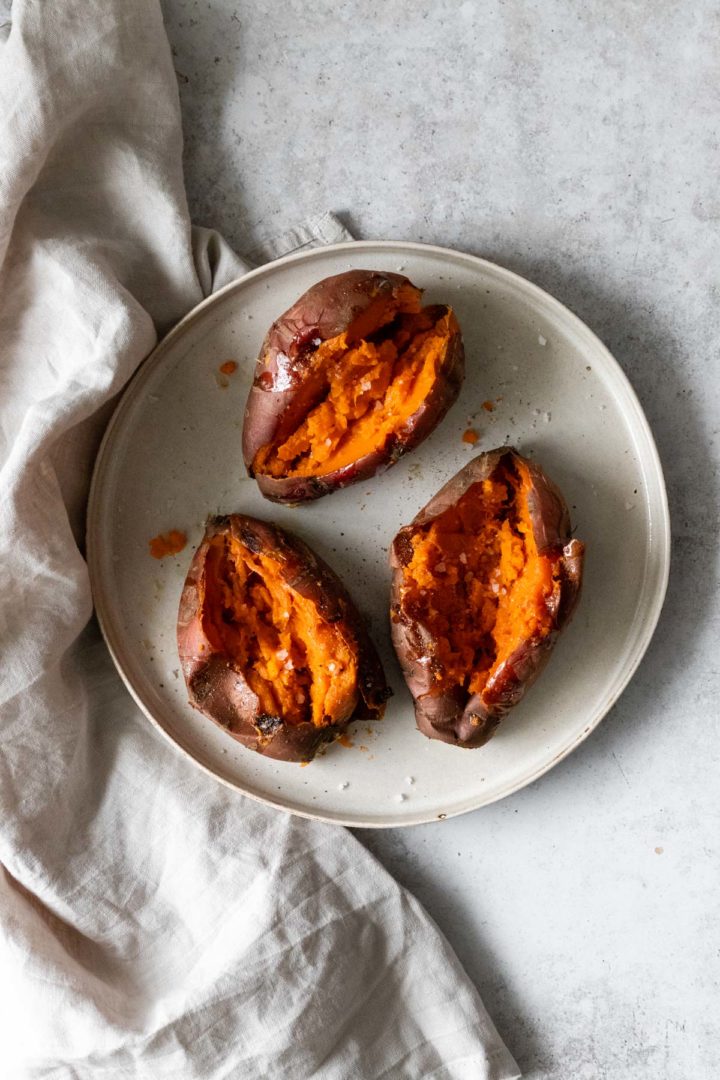 three baked sweet potatoes on a plate seasoned with salt and black pepper